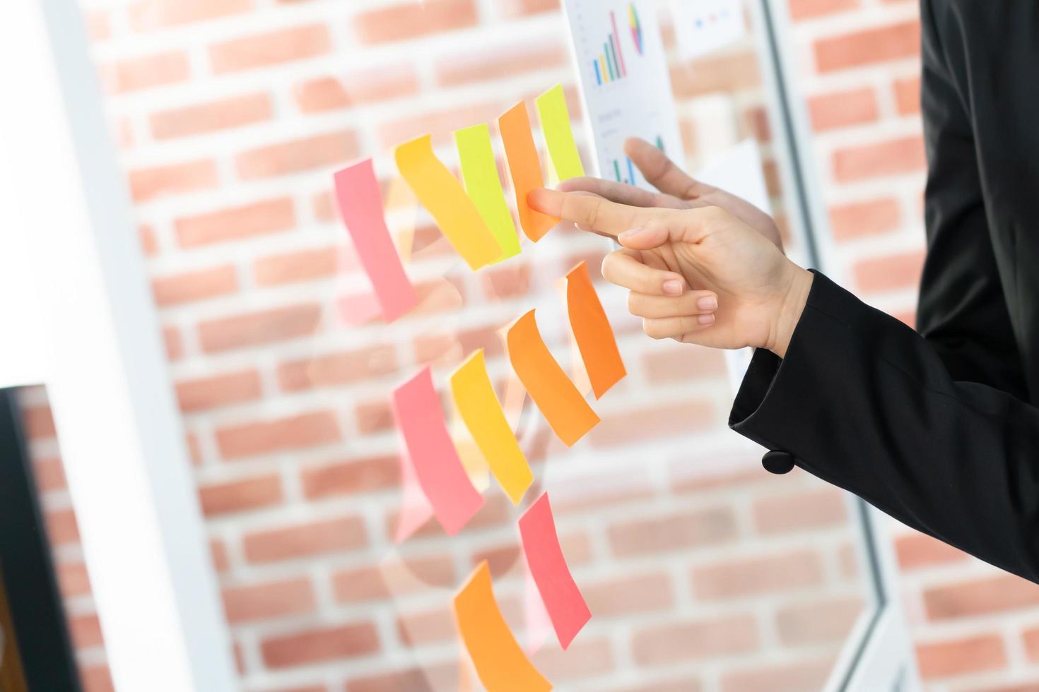 pointing on glass wall with glued colorful paper notes. Note paper reminder schedule board. Business people meeting and use post it notes to share idea. Discussing - business, teamwork, concept photo