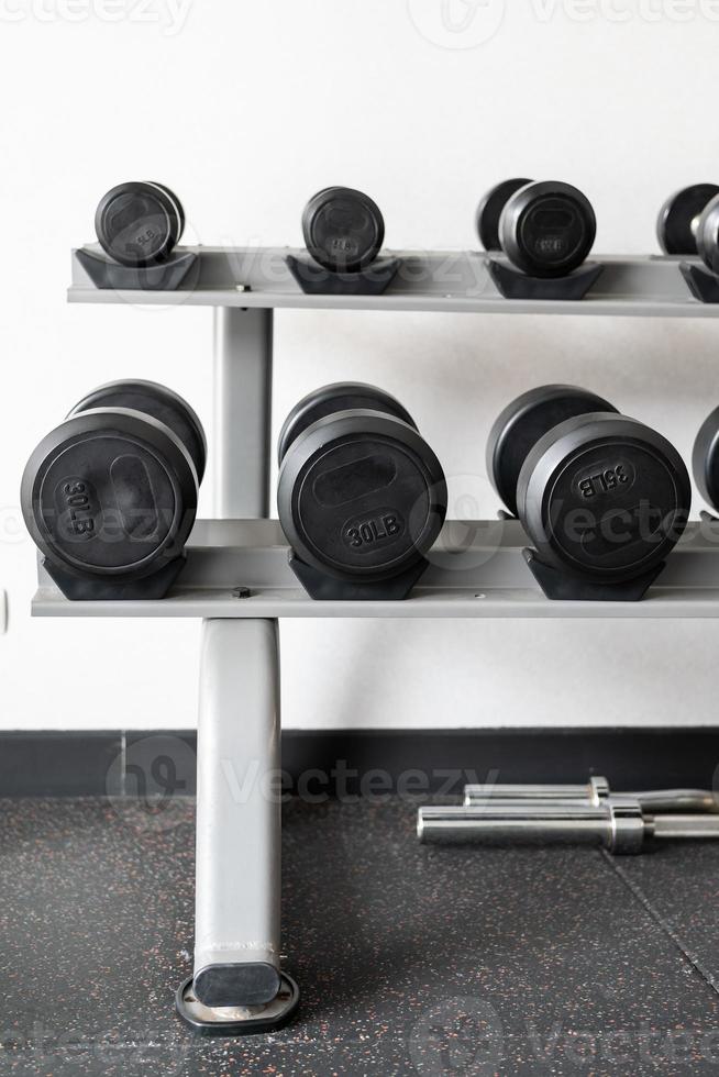 Stand with dumbbells. Sports and fitness room. Weight Training Equipment. Black dumbbell set, many dumbbells on rack in sport fitness center photo