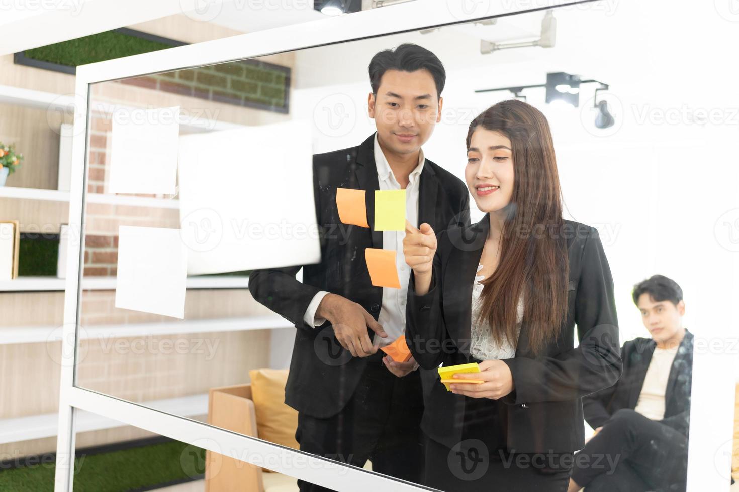 businesspeople office worker reading sticky notes on planning glass board. Business team pointing on keywords in sticky notes and business report to brainstorming about planning strategy of business. photo