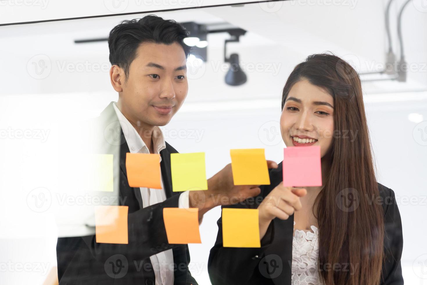 businesspeople office worker reading sticky notes on planning glass board. Business team pointing on keywords in sticky notes and business report to brainstorming about planning strategy of business. photo