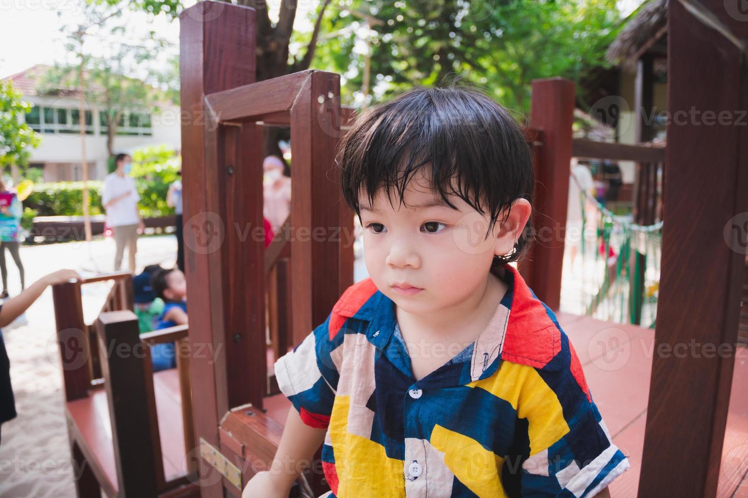 Asian boy play at outdoor playground. During summer or spring. Child felt hot and sweaty on his face. Taking care of health of young kid in hot weather. Baby 2-3 year old. Children wear colorful dress photo