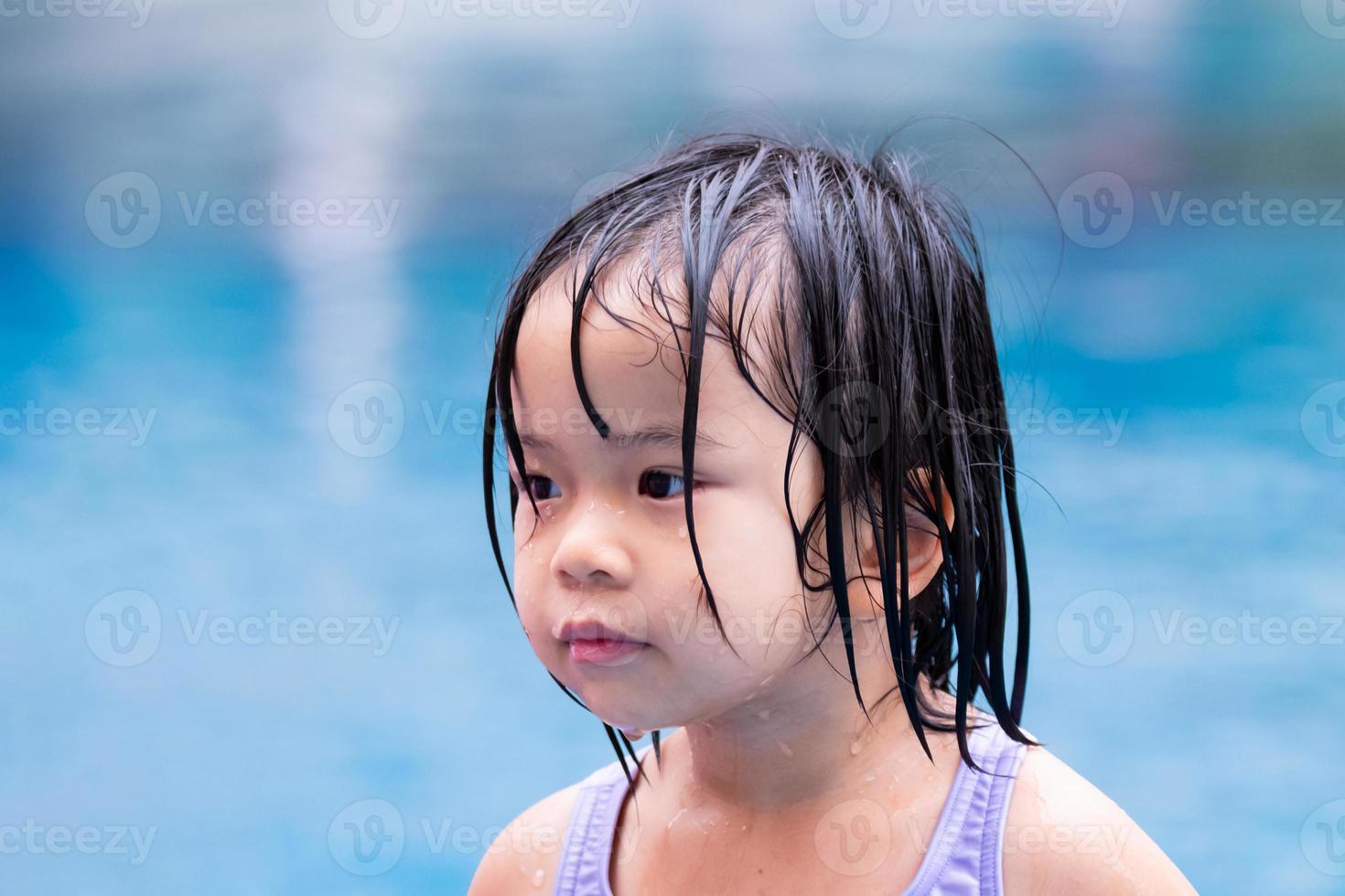 Closeup child face aged 4-5 years old. Girl got wet from playing in clear blue pool. Children are happy. During  summer or spring. Travel at resort. Empty space. photo