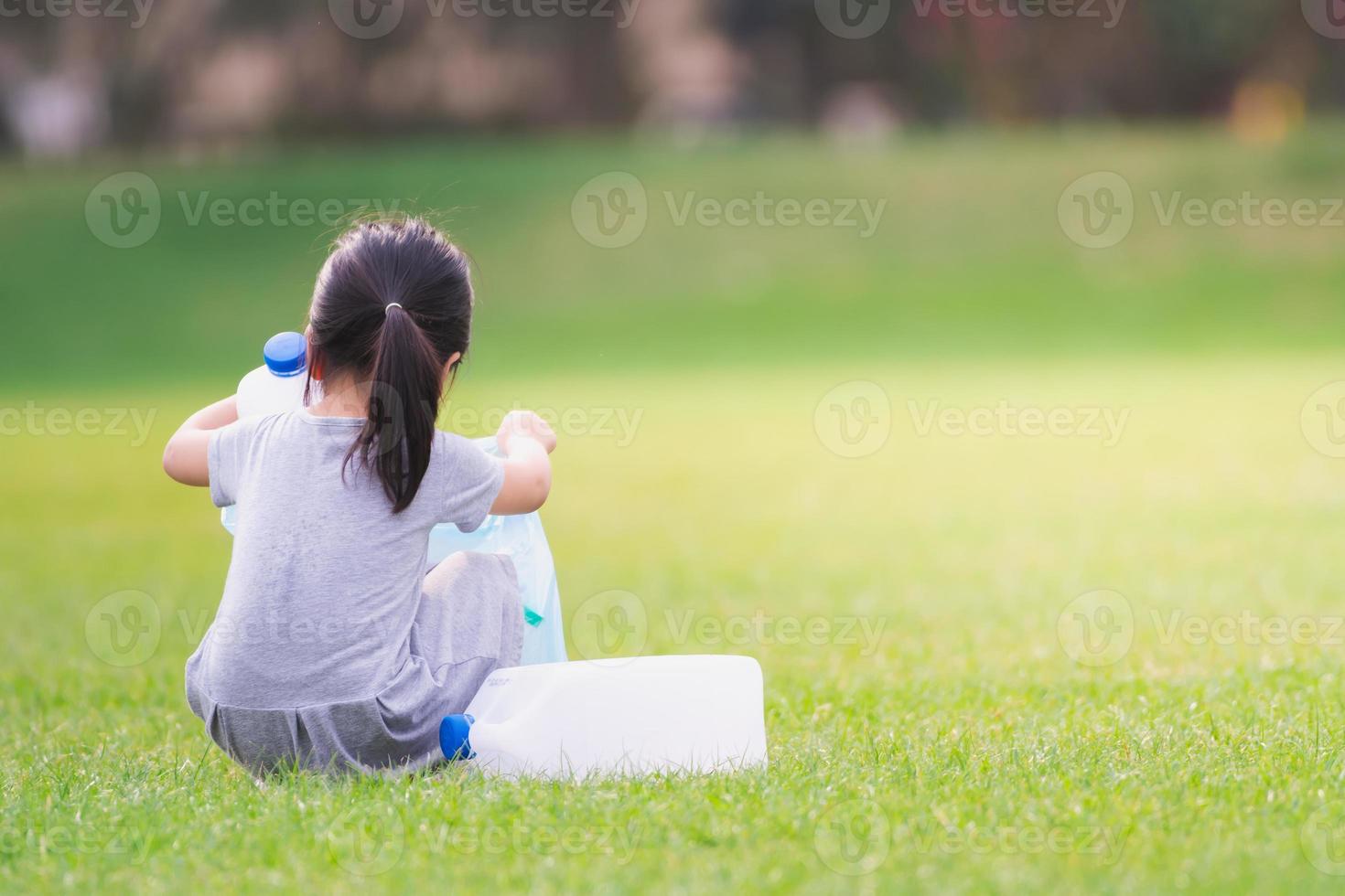 Rear view of  4 year old Asian girl is picking up trash plastic bottle in a green lawn. Environmental concept. photo