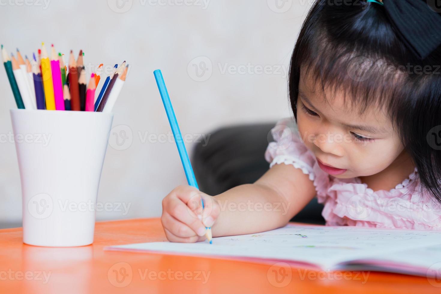 A 4-5 year old Asian girl is working hard on her assignment. Children sit and write homework. Children study at home. Sit at the desk and study. photo