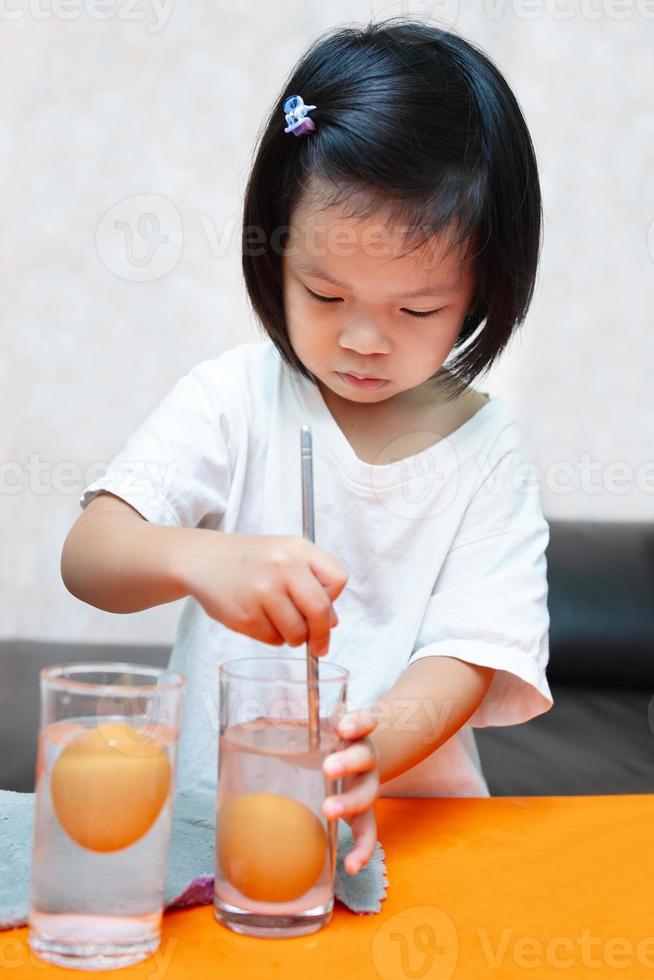 Student learning and doing principles science experiments. Sinking Egg Experiment - Floating eggs with water and salted water. Girl is using metal rod stir to dissolve salt in water. Doing it yourself photo