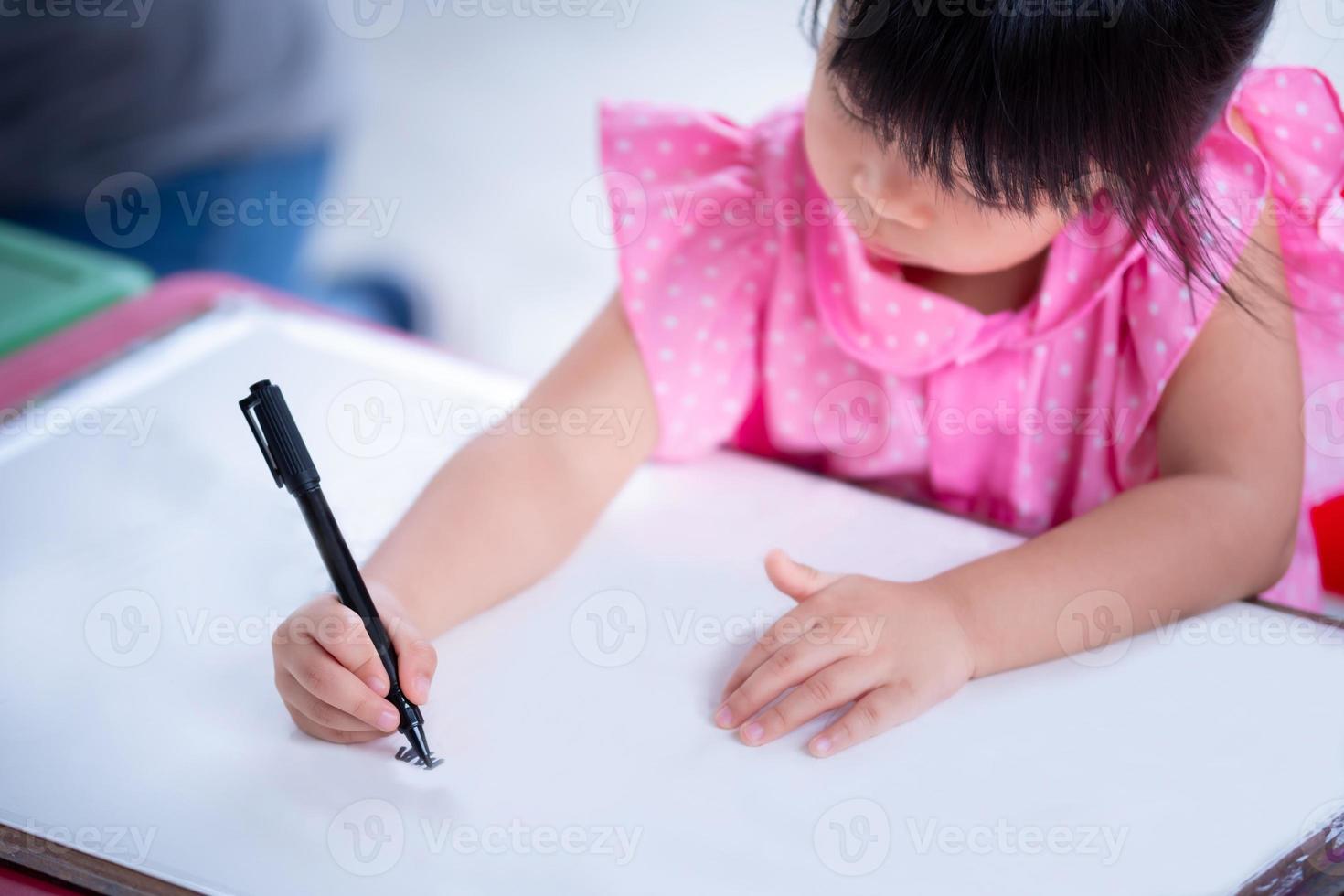 Selective focus child hand holding magic pen. Asian cute girl doing art on white paper. Happy kid learning craft homeschool. Student doing homework. Hobby time kindergarten. Female aged 4 years old. photo