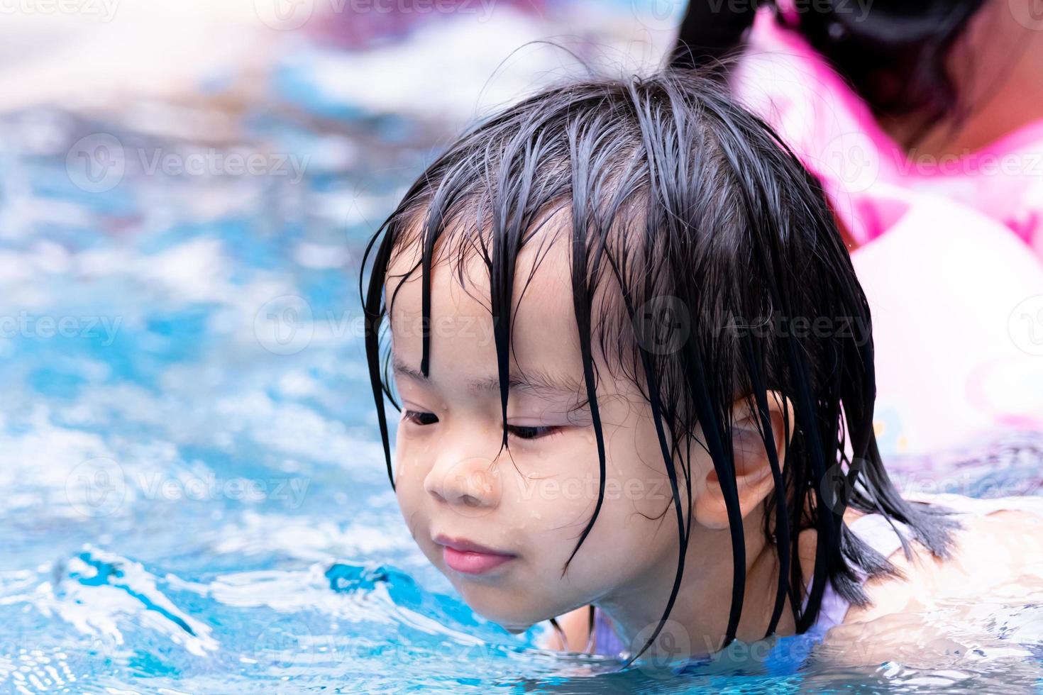 Head shot. Asian child girl playing water in the pool. Family travel resort in holiday. Portrait of baby like swimming. Happy kid aged 4-5 years old. Exercises that children love. Summer time. photo