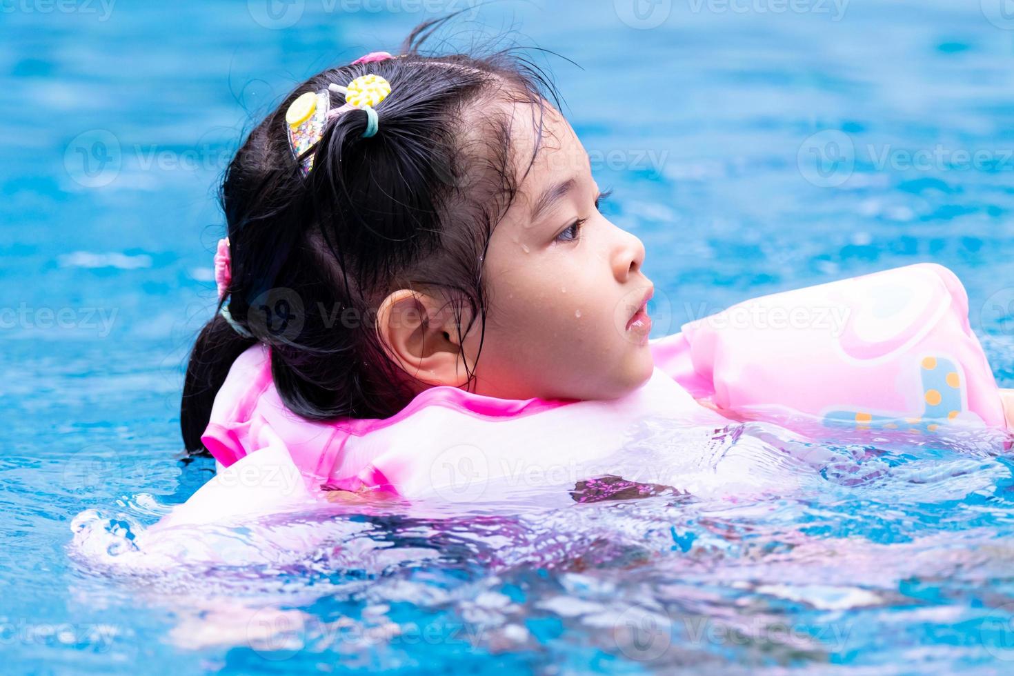 niña asiática nadando en la piscina. niño con chaleco salvavidas rosa. estuario de seguridad. Hora de verano. los niños hacen ejercicio. bebé de 4-5 años. foto