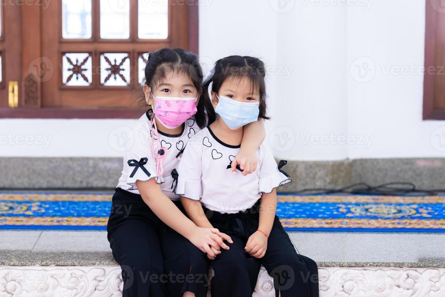 Portrait cute children girl wearing face mask. Sister hugs sister's neck. Happy kid sweet smile and looking at camera. Child aged 4-5 years old. photo