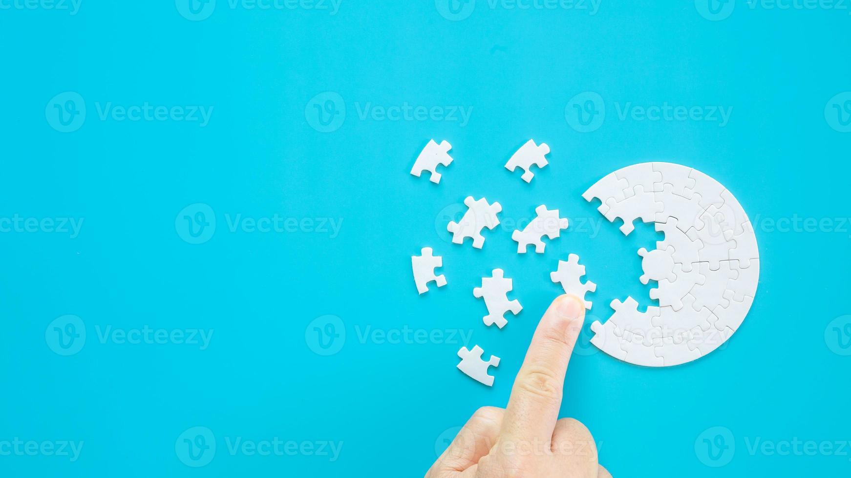 Close up hand holding and playing jigsaw game incomplete. White part of jigsaw puzzle pieces on blue background. concepts of problem solving, business, teamwork, Texture photo with copy space for text