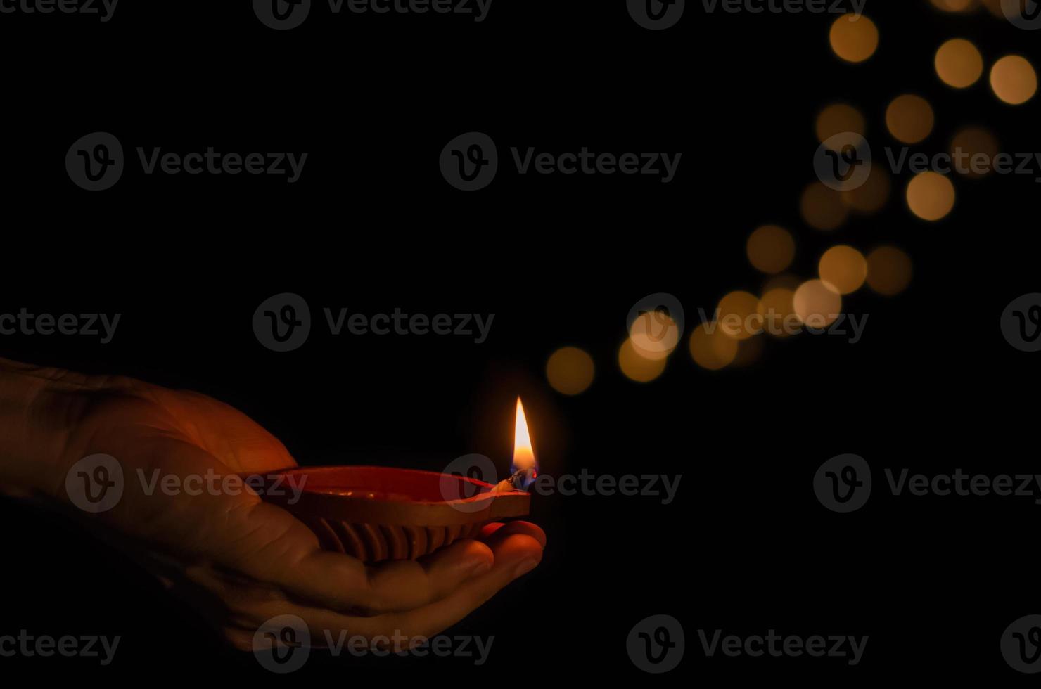 Hand holding the clay diya lamp lit on dark background with bokeh lights. Diwali festival concept. photo