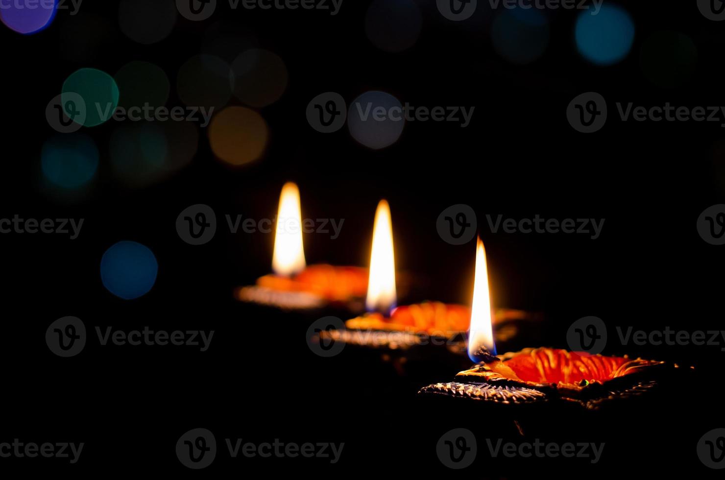 Selective focus on flame of clay diya lamps lit on dark background with colorful bokeh lights. Diwali festival concept. photo