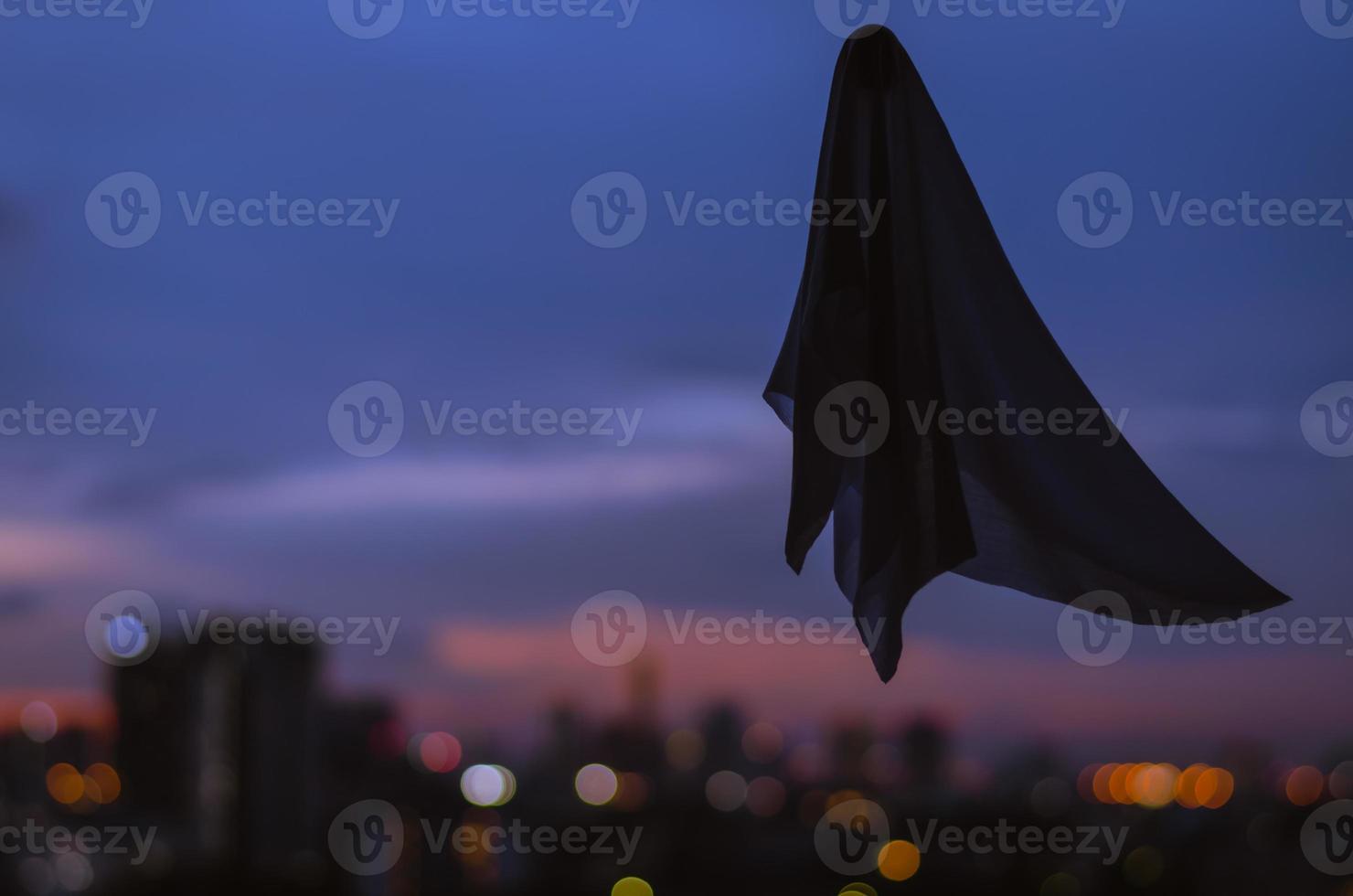 Ghost sheet flying in dusk sky with city lights background. Halloween scary concept. photo