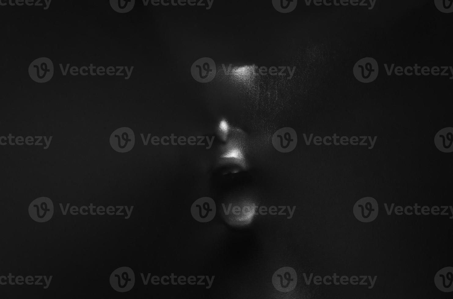 Screaming human face pressing through black fabric with shine and dark side for Halloween background concept. photo
