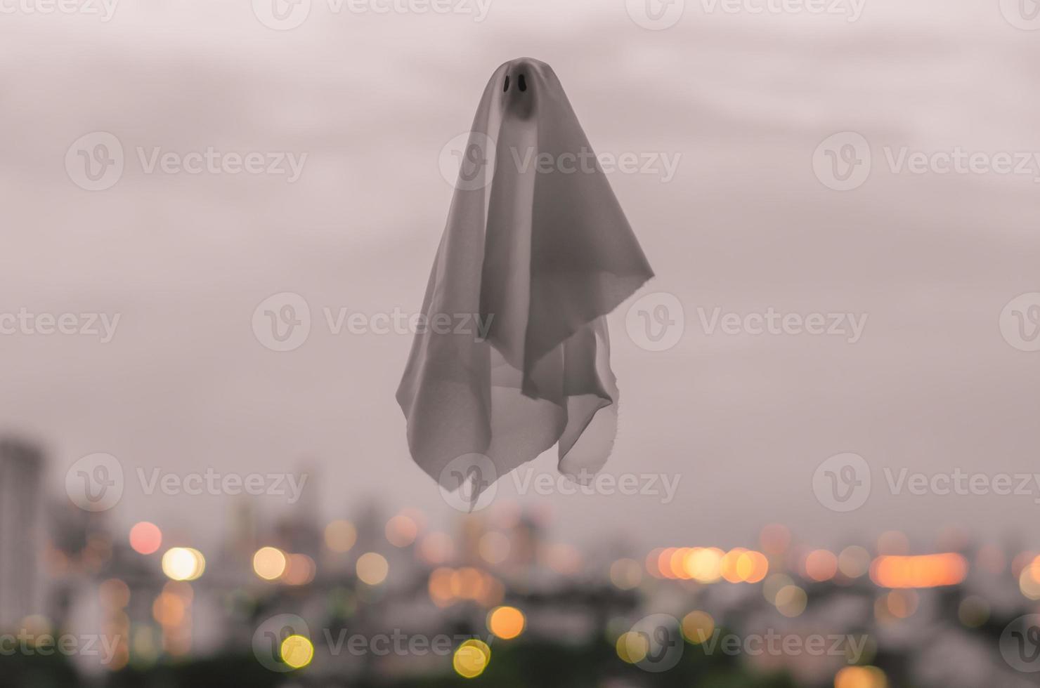 White ghost sheet flying in dusk sky with city lights background. Halloween scary concept. photo