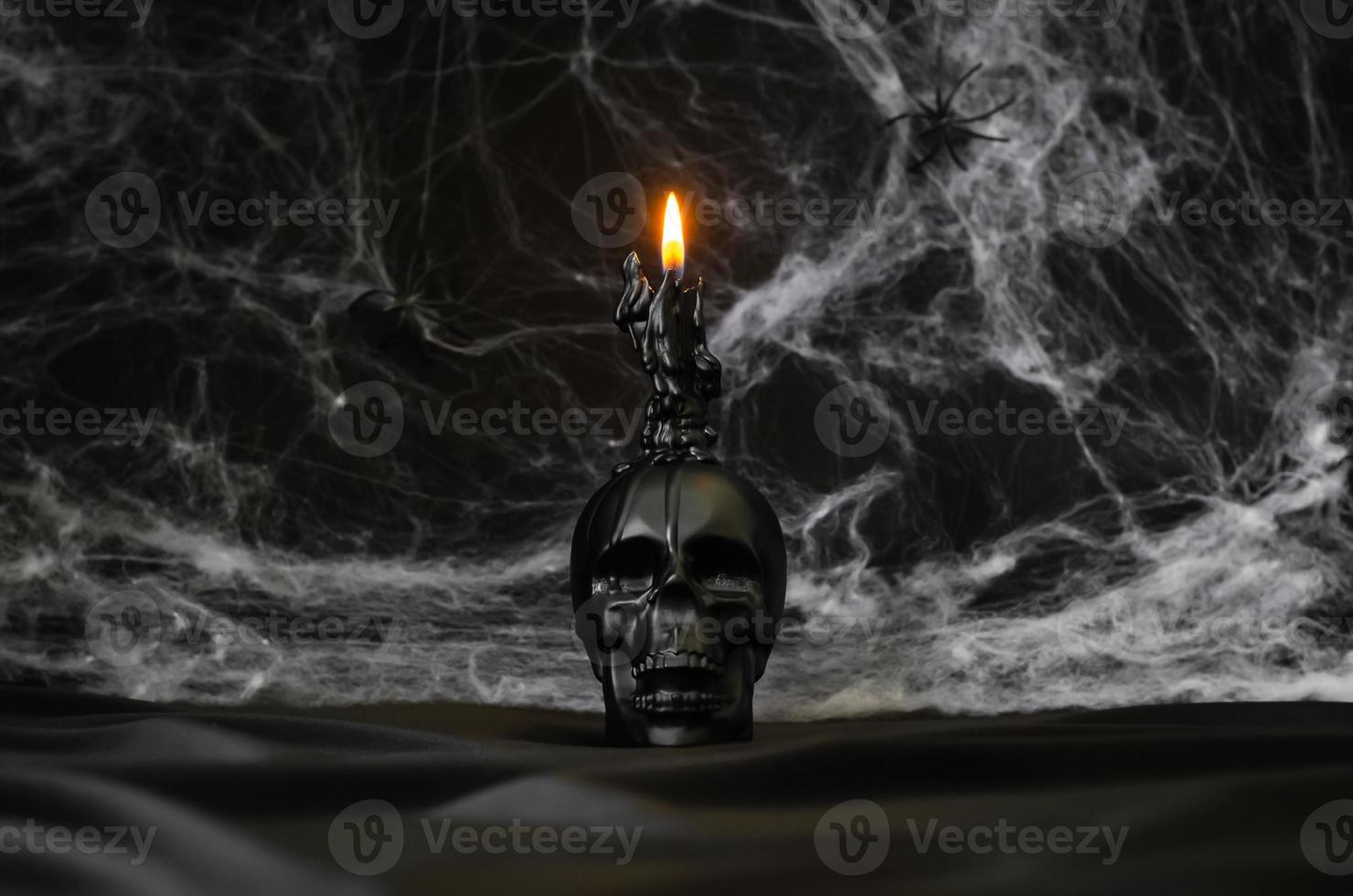 Scary halloween background with skull that have candle on top puts on black satin fabric with cobweb. photo