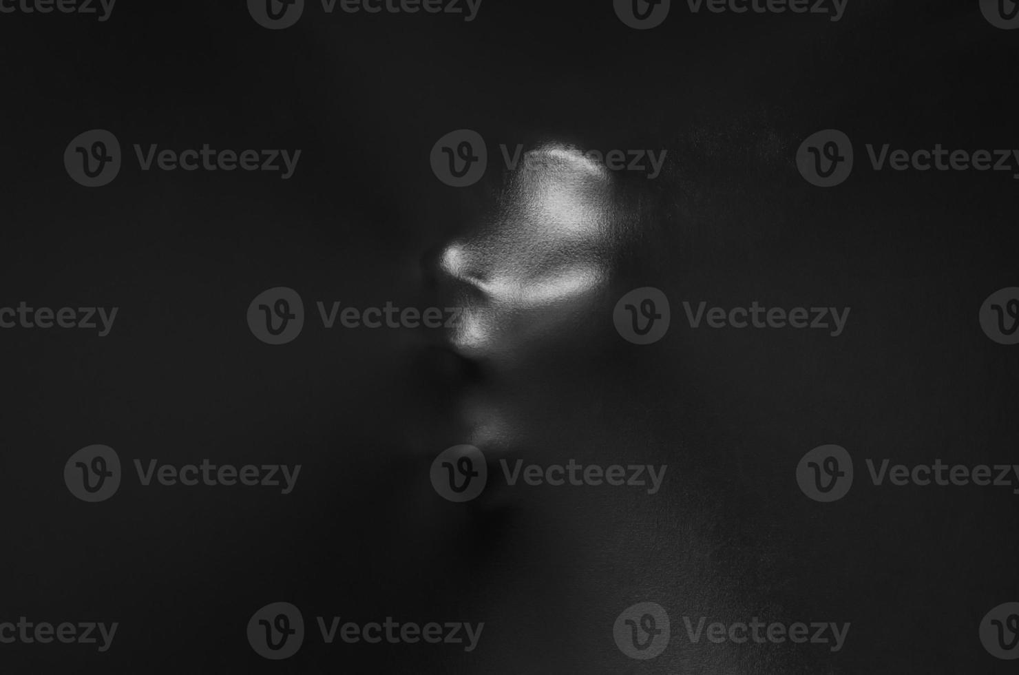 Screaming human face pressing through black fabric with shine and dark side for Halloween background concept. photo