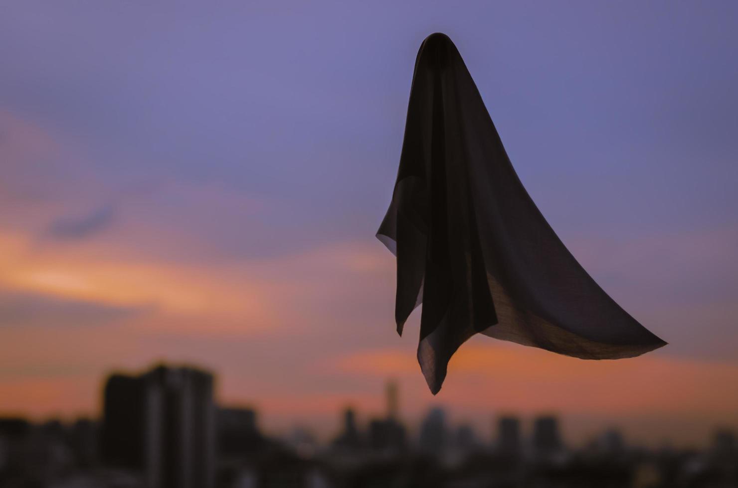 Ghost sheet flying in dusk sky with city lights background. Halloween scary concept. photo