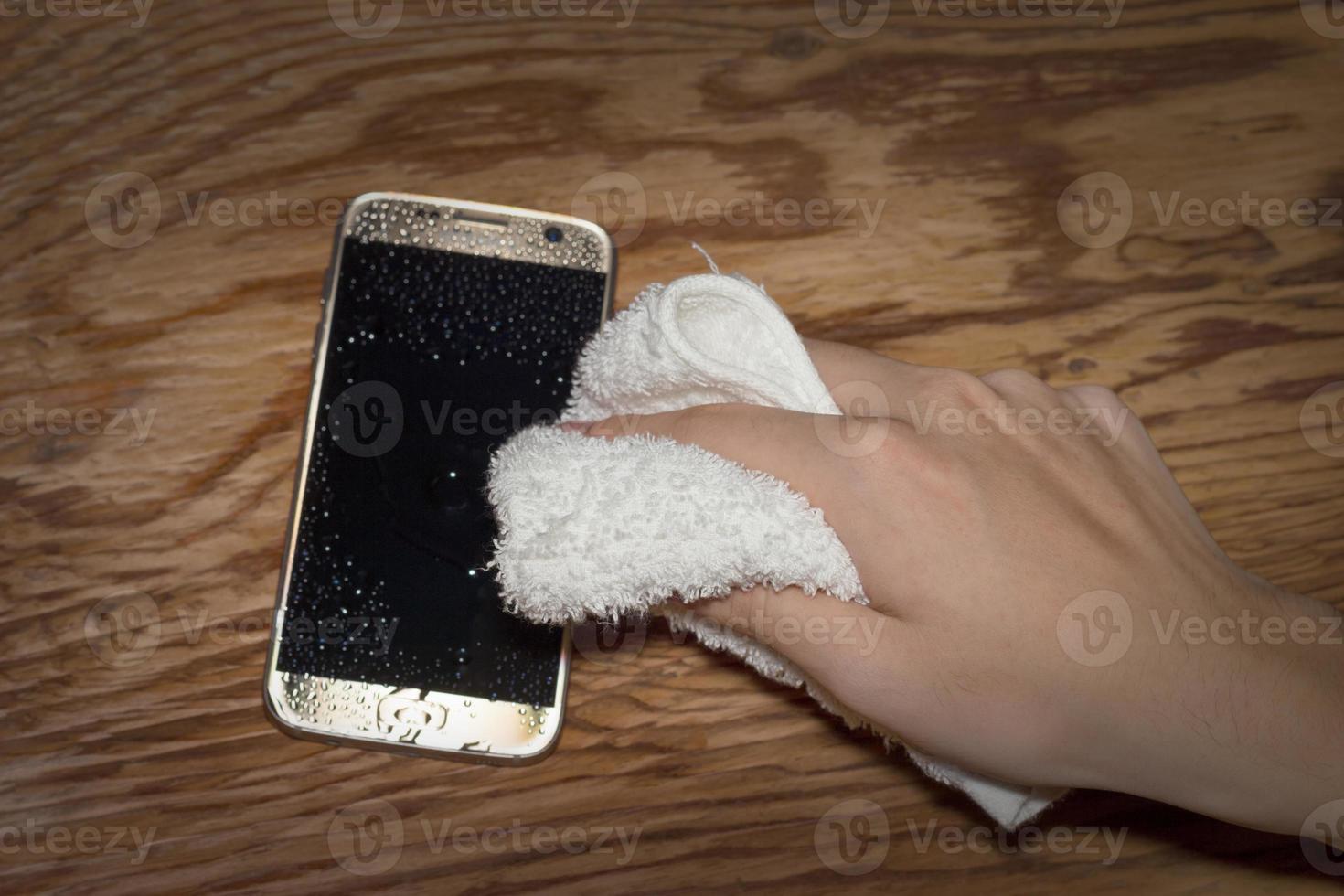 Hands holding White cloth with wet smartphone drops on wooden floor photo