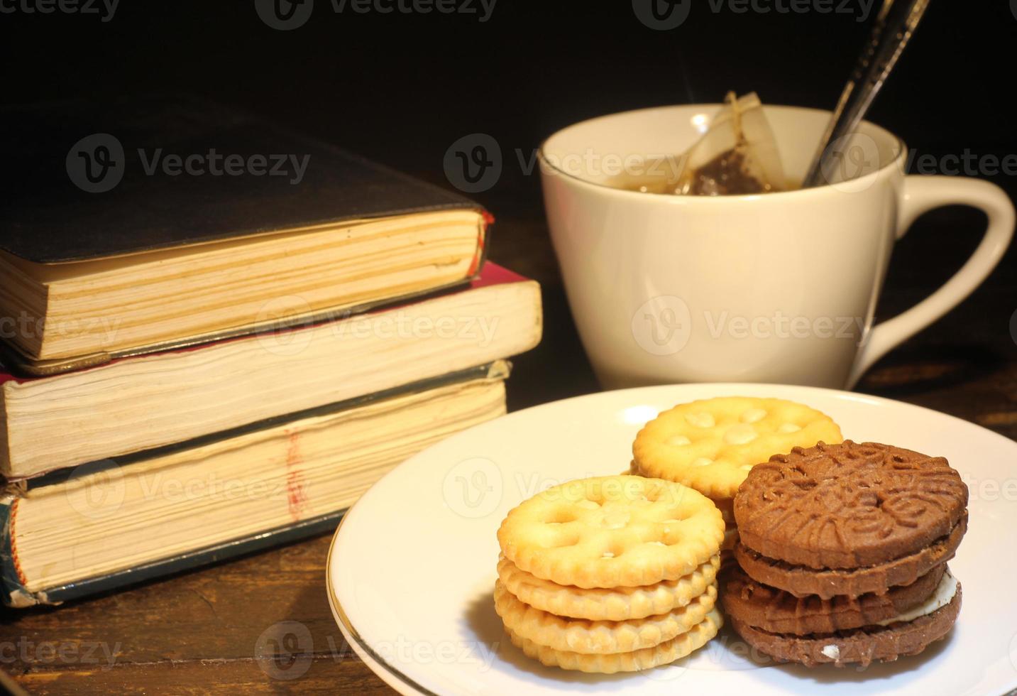 cup of tea with small spoon, biscuit on a plate and a stack of books on the table selective focus photo