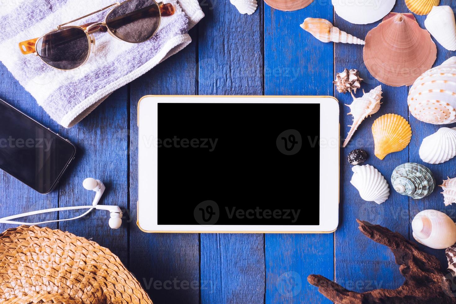 Top view of Gadget with accessories for summer trip and seashells on blue painted wood plank background. photo