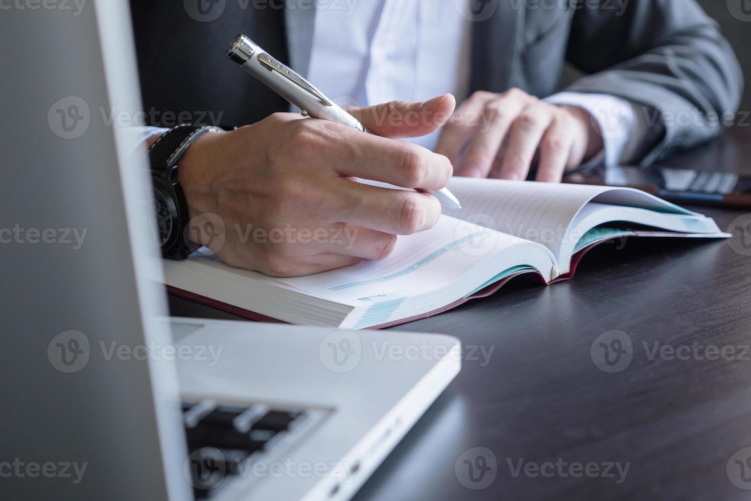 Close up of businessman writing note and using a laptop on the office desk. photo