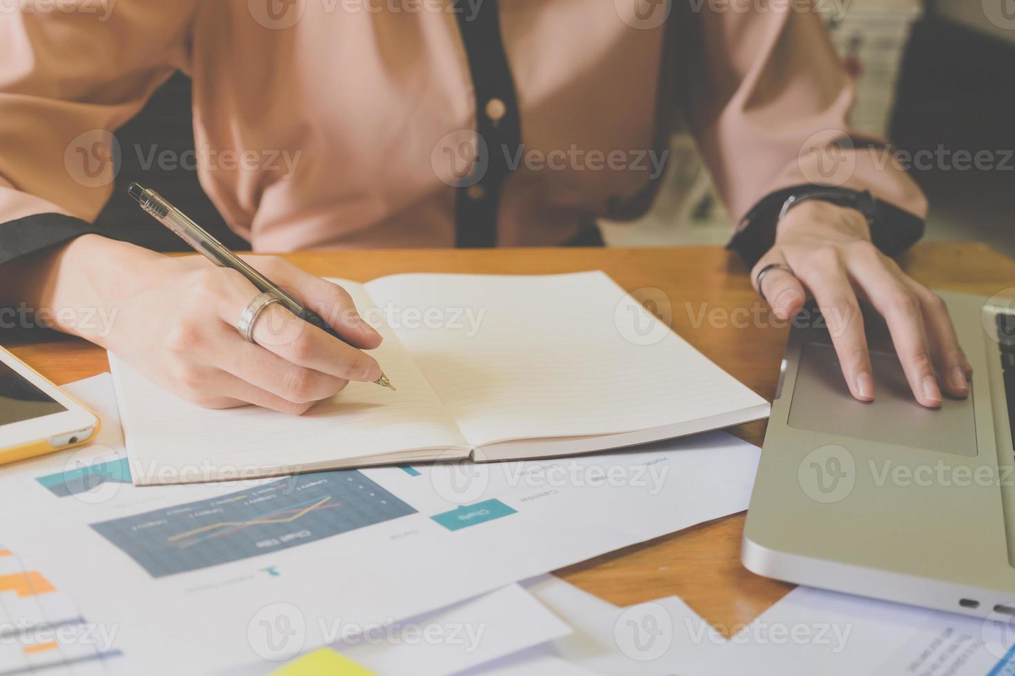 Close up of female hands writing some data in notebook and using laptop on the office desk. photo