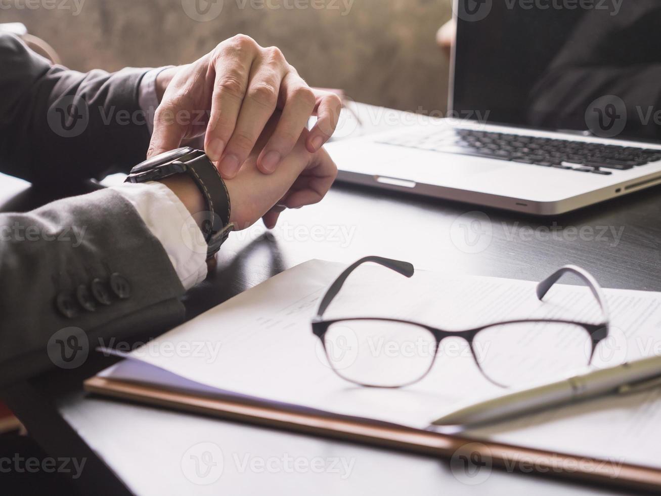 primer plano de un hombre de negocios que trabaja en el escritorio y revisa la hora en su reloj de pulsera. foto