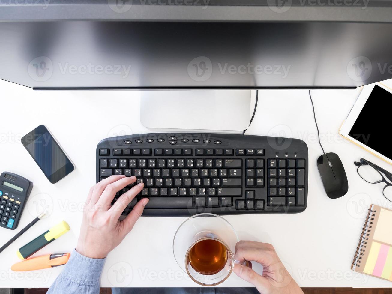 Top view of male hands working on computer and holding tea cup on the desk. photo