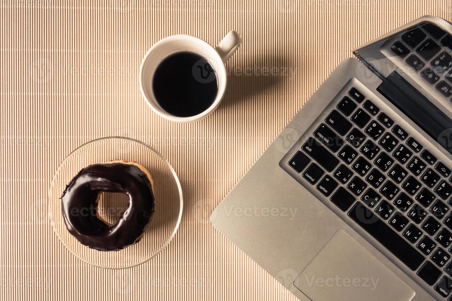 Top view of laptop with coffee cup and donut on table. photo