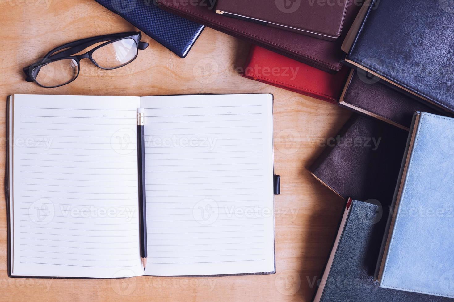 Blank notebook with pencil, glasses and books on wooden table. photo