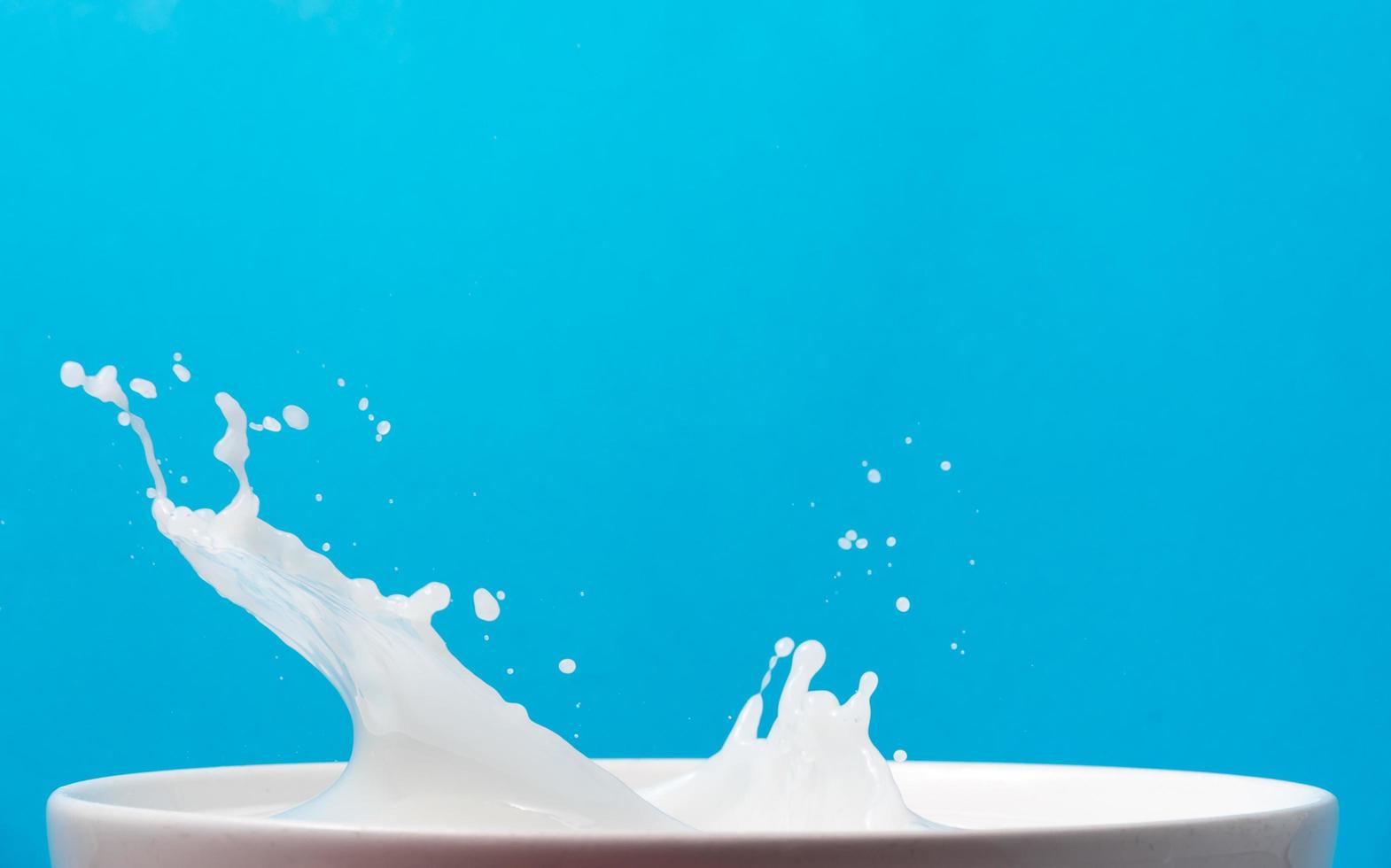 chorrito de leche de una taza sobre fondo azul. foto