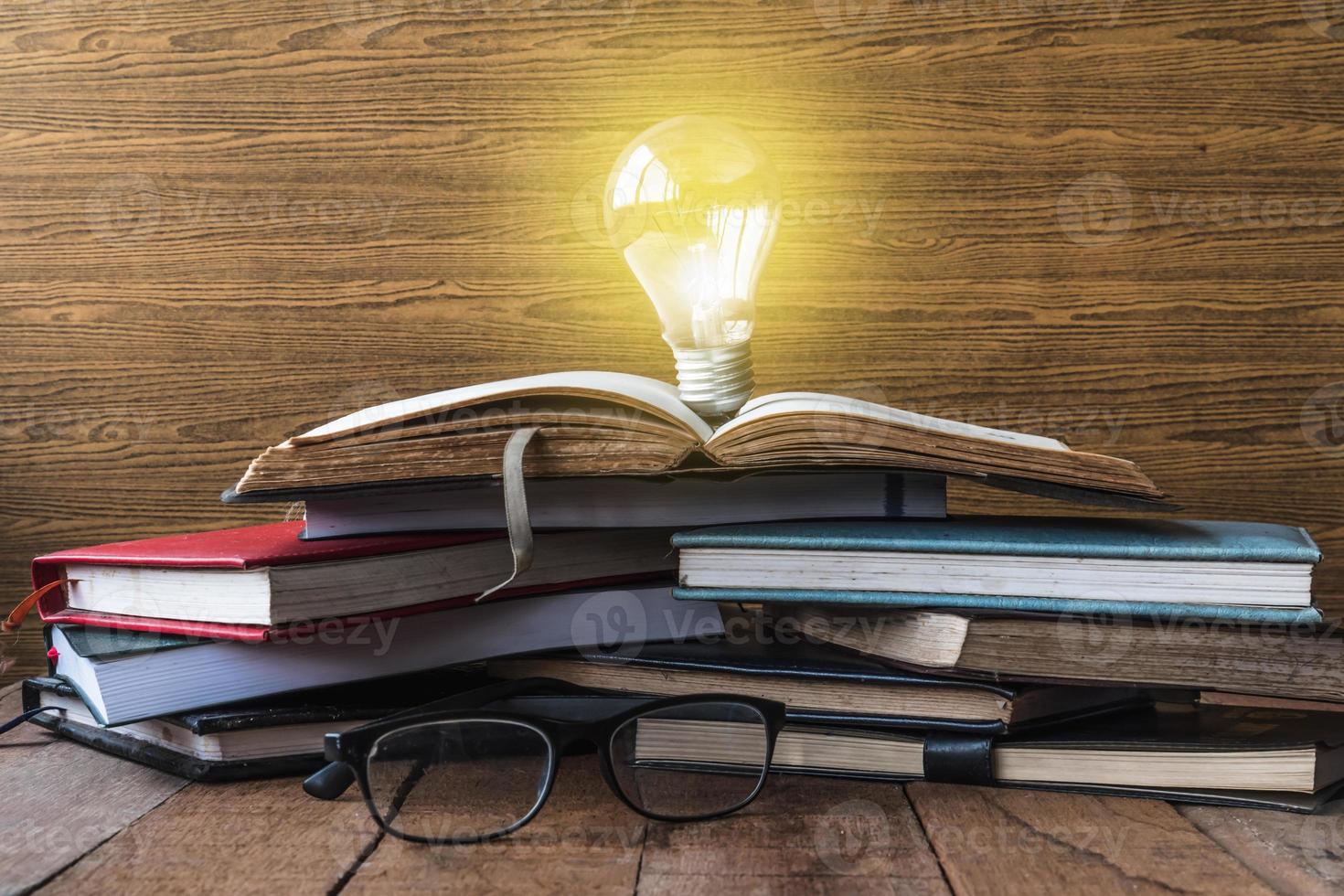 Open book with light bulb, hardback books and glasses on wooden table. photo