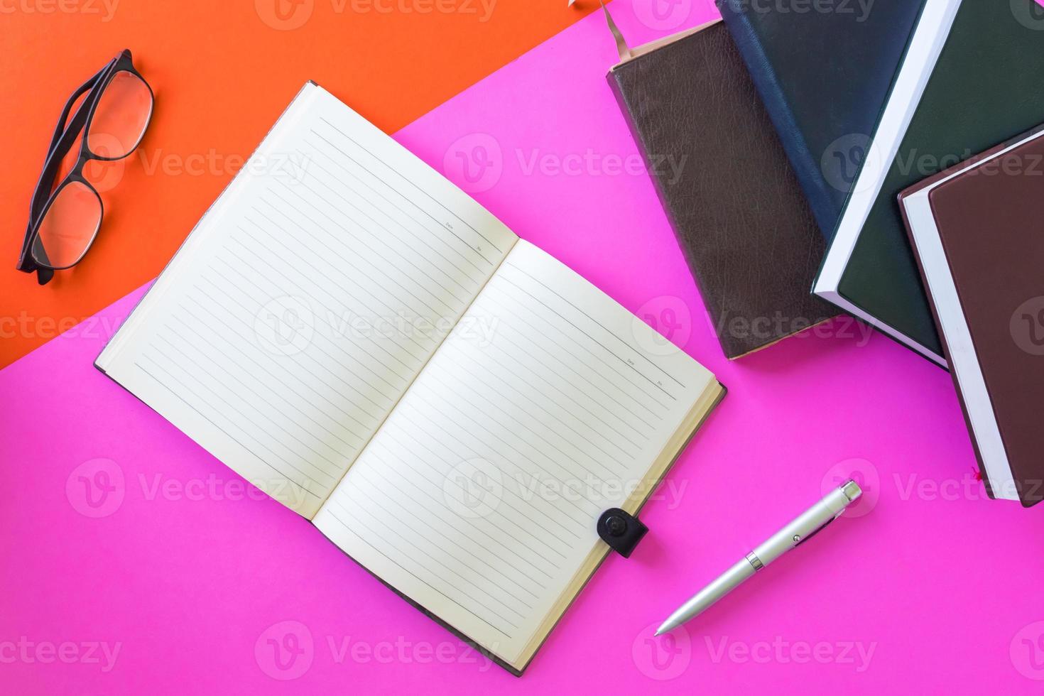 Open blank notebook with pen, glasses and hardback books on colorful background. photo