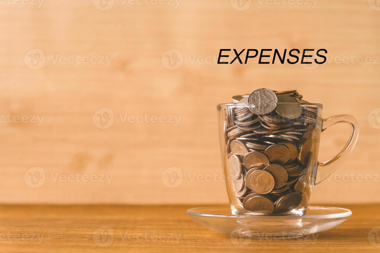 monedas en una taza con texto de gastos en la mesa de madera. concepto financiero. espacio libre para texto foto