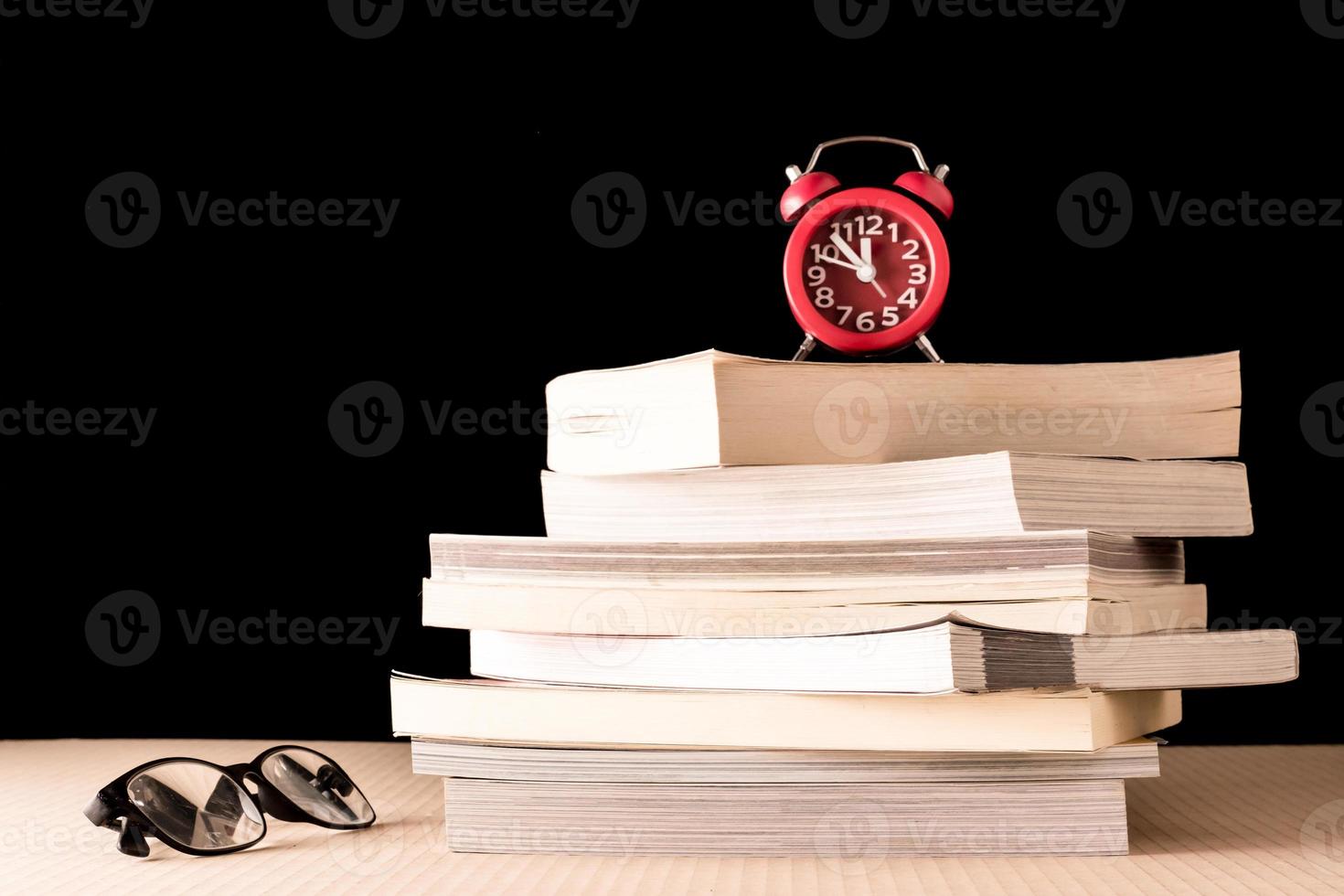 Stack of books with eyeglasses and clock on wooden table, Black background photo
