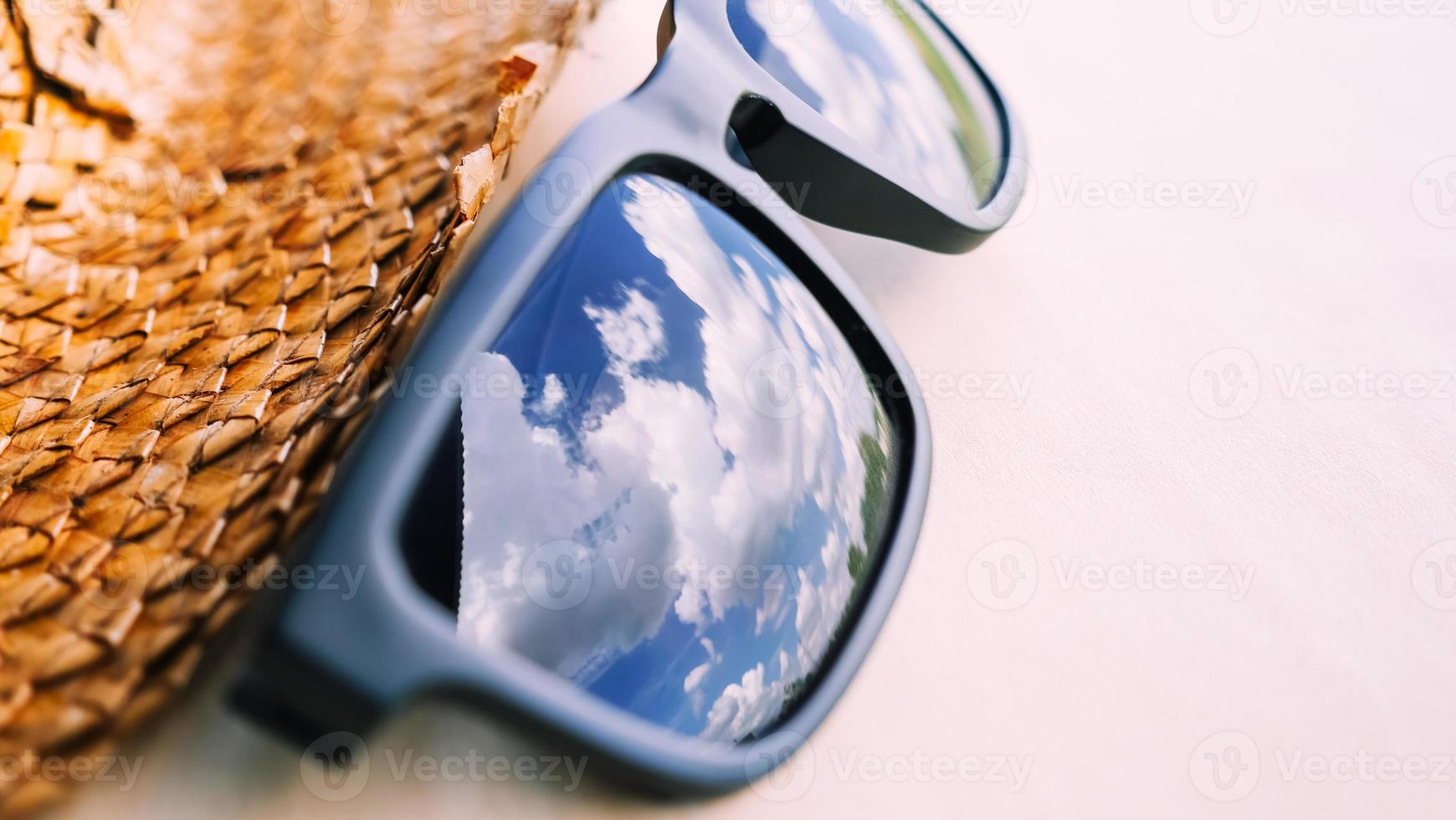 gafas de sol con el reflejo del cielo azul y sombrero sobre la mesa, enfoque suave. foto