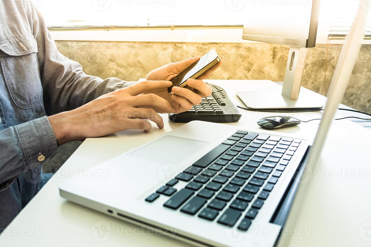 Male hands using smart phone with computer on the desk. photo