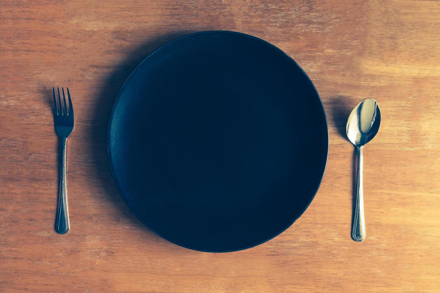 Top view of empty black plate with spoon and fork on wooden table photo