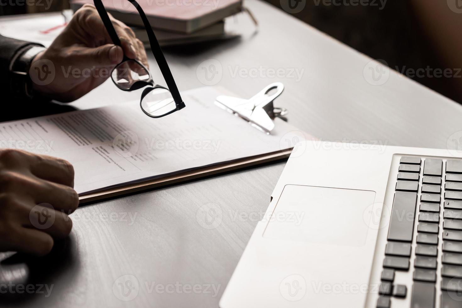 Close up of businessman holding eyeglasses and reading documents on the office desk. photo