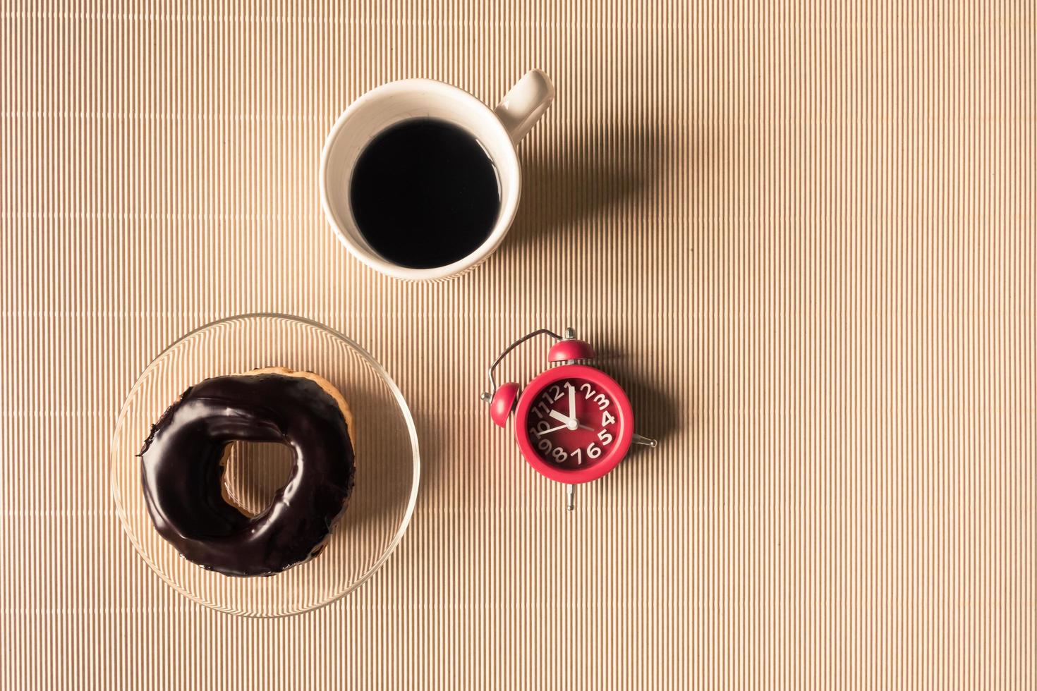 Top view of coffee cup with donut and clock on table. photo