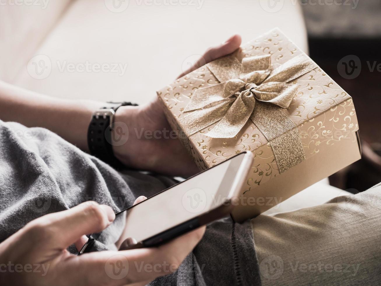 cerca de las manos de un hombre casual usando un teléfono inteligente y sosteniendo una caja de regalo. foto
