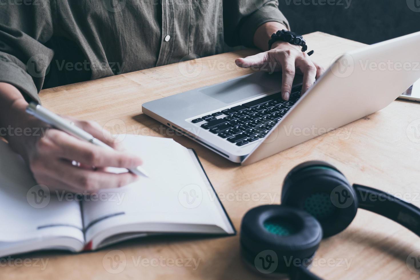 Close up of casual man writing note and using laptop on the desk. photo