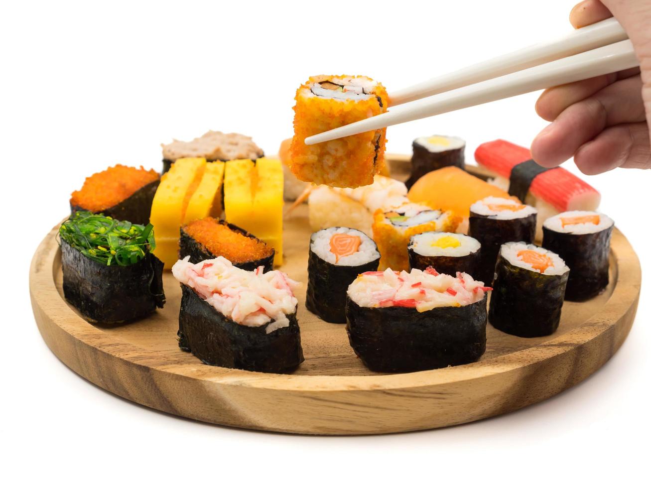 mano sosteniendo rollo de sushi con palillos, sushi en placa de madera sobre fondo blanco, comida japonesa. foto