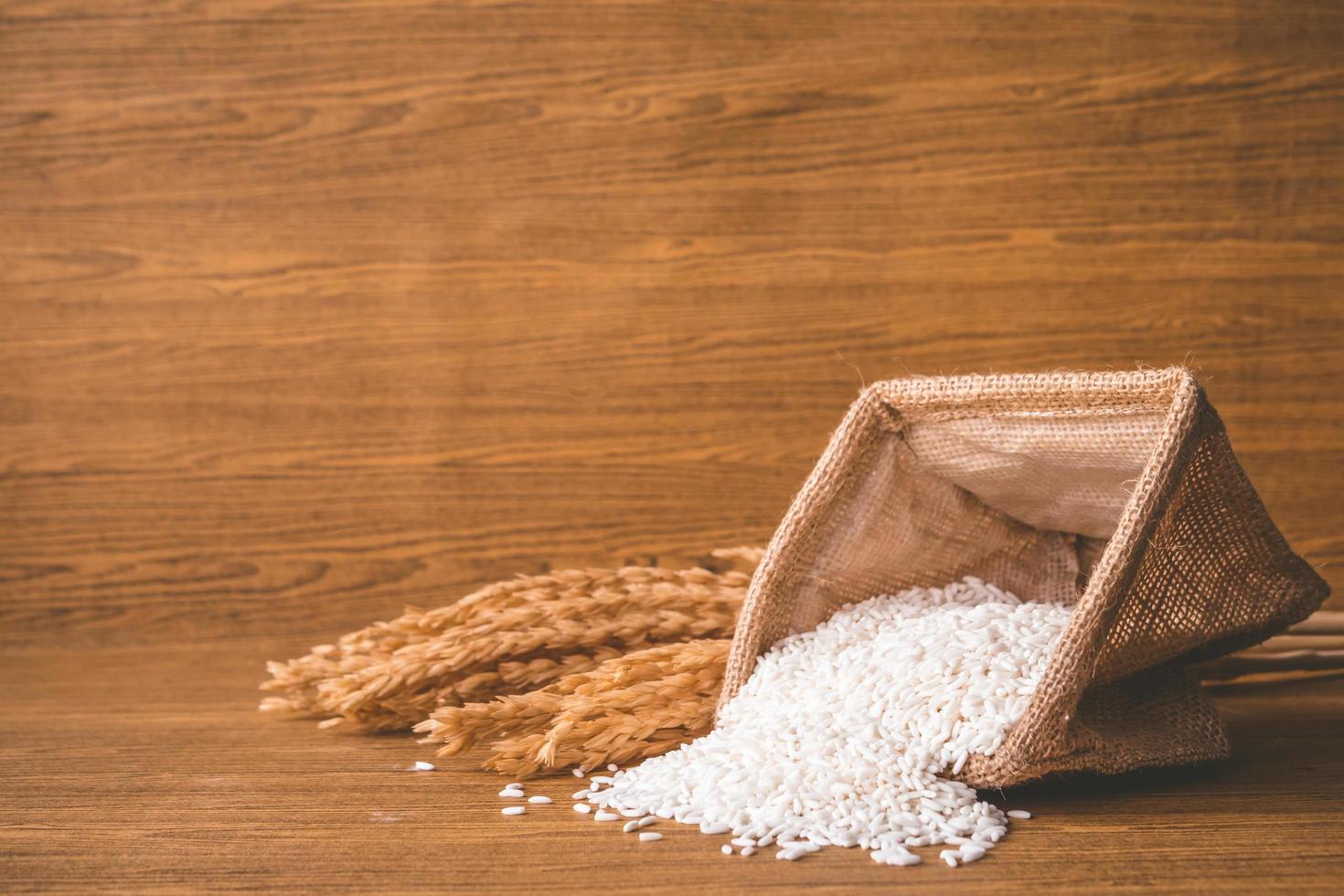 Close up of raw rice in burlap sack on wooden table. photo