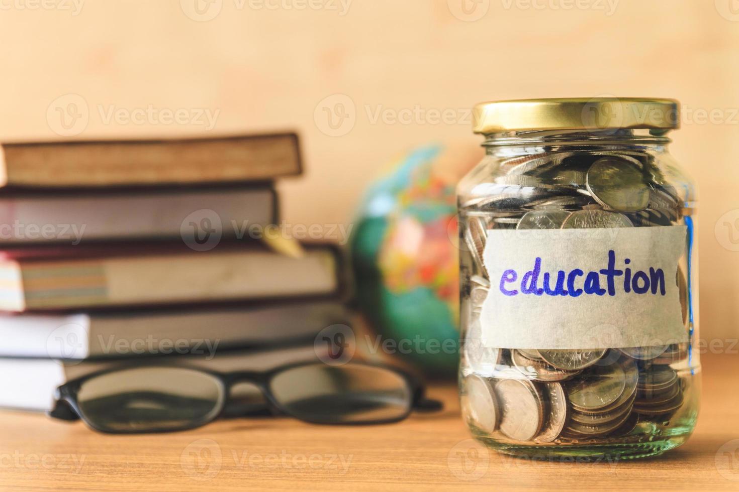 monedas en frasco de vidrio con etiqueta de educación, libros, vasos y globo sobre mesa de madera. concepto financiero. foto