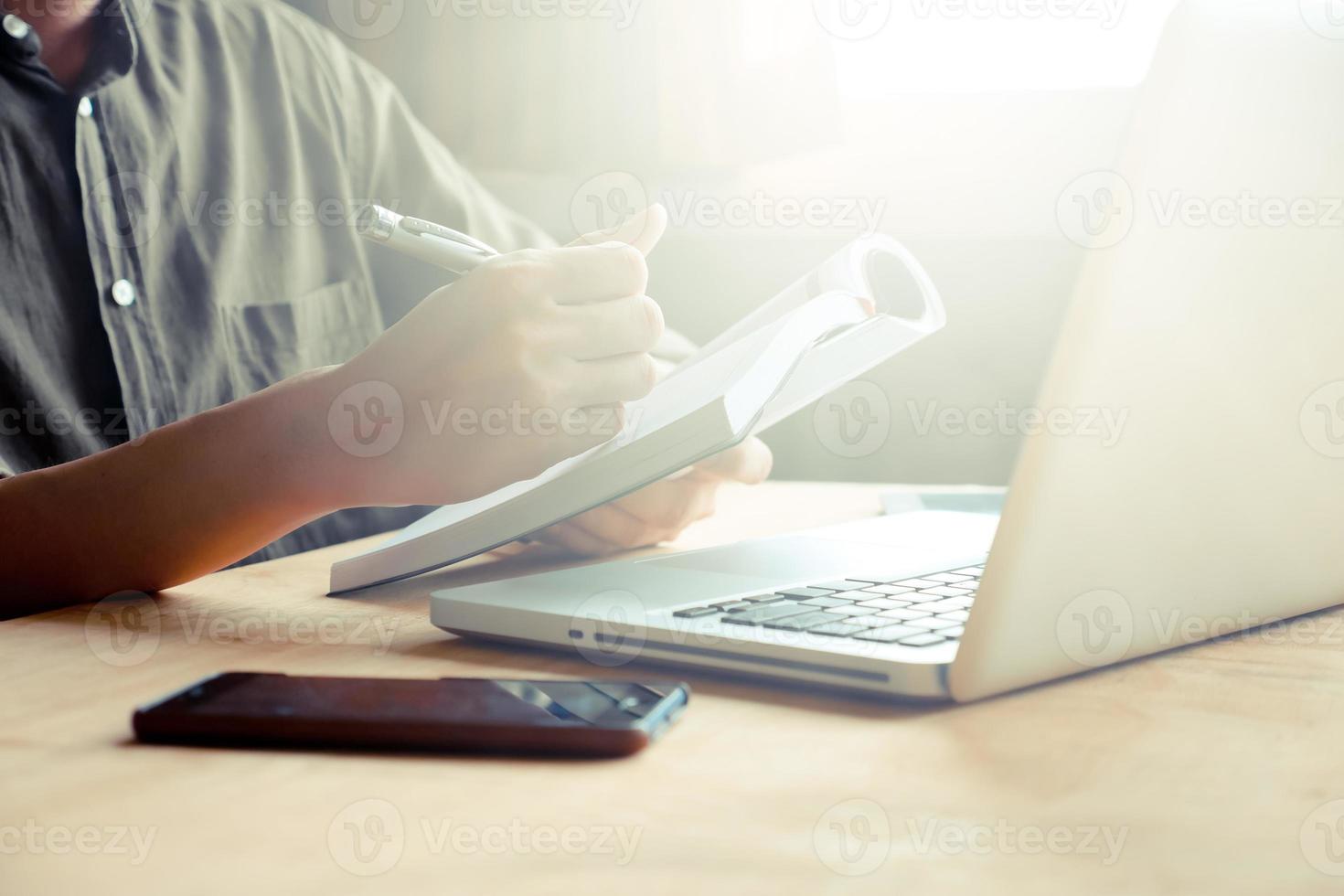 Close up of casual man writing note and using laptop on the desk, toned with sunlight photo