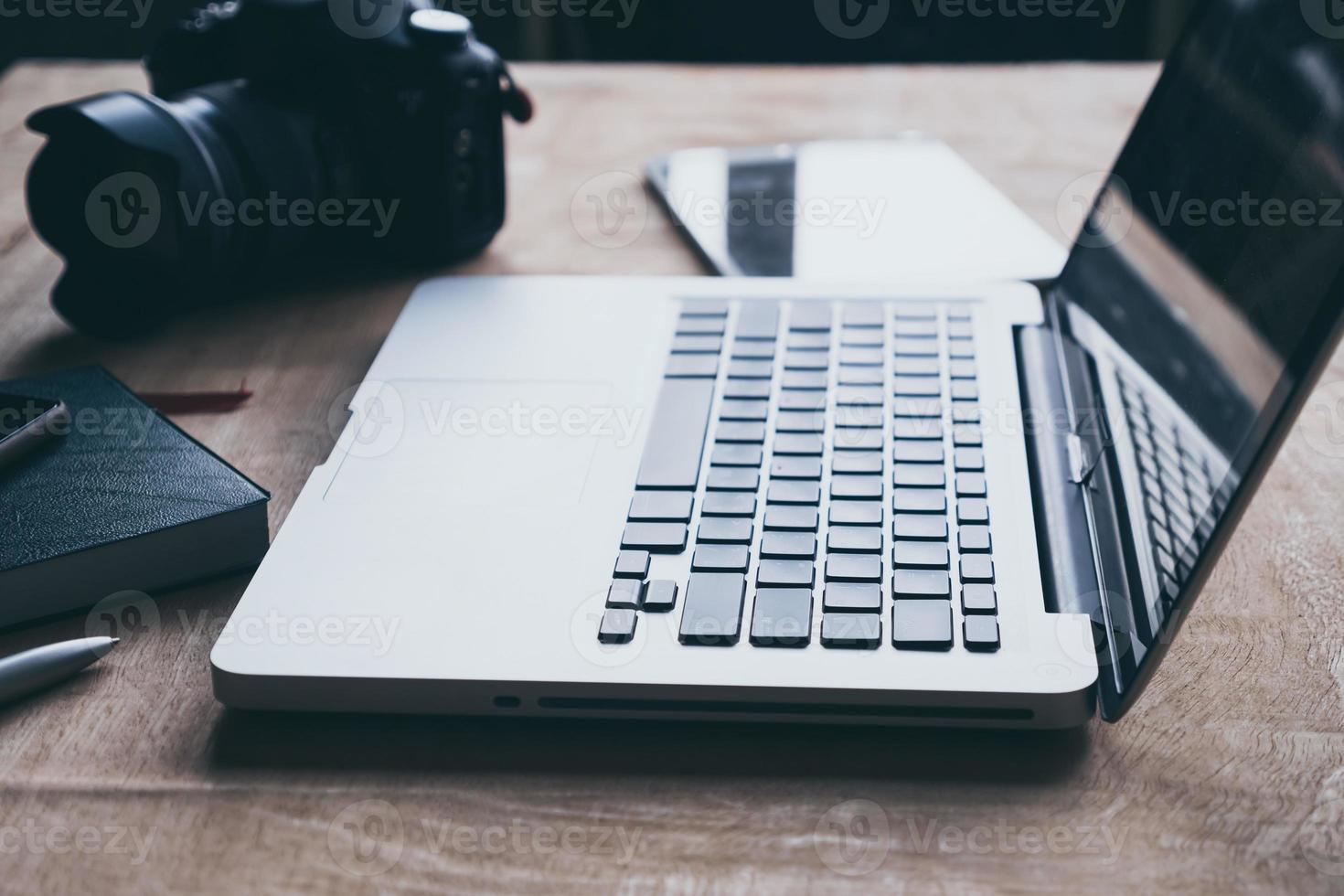 Laptop with tablet and camera on wooden table. photo