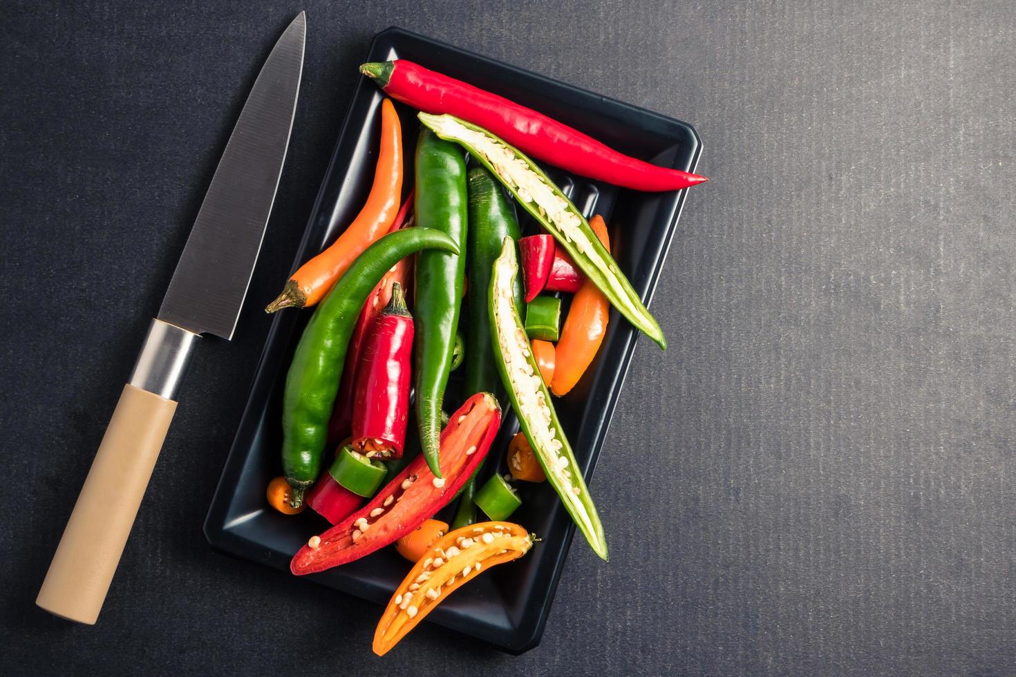 Colorful mix of chili pappers with knife on  black background. Free space for text photo