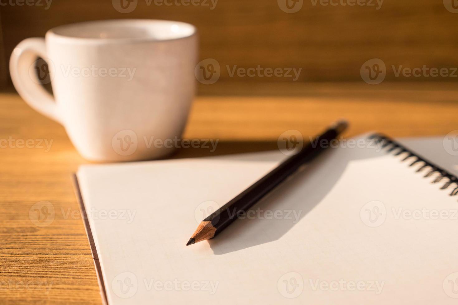 Blank notebook with pencil and coffee cup on wooden table background. Selective focus photo